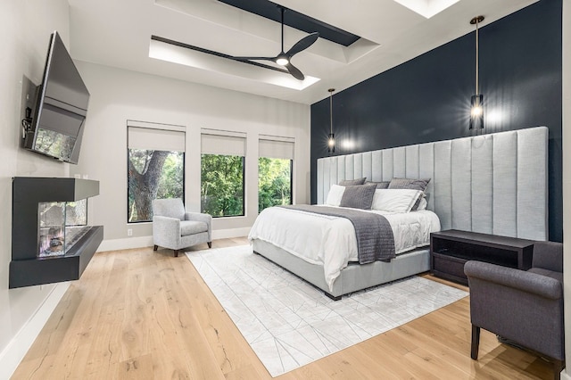 bedroom featuring ceiling fan, light wood-type flooring, and a tray ceiling