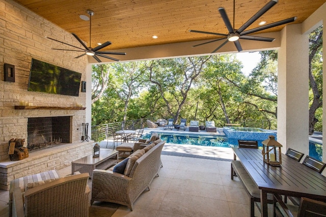 view of patio featuring an outdoor stone fireplace, ceiling fan, and a pool with hot tub