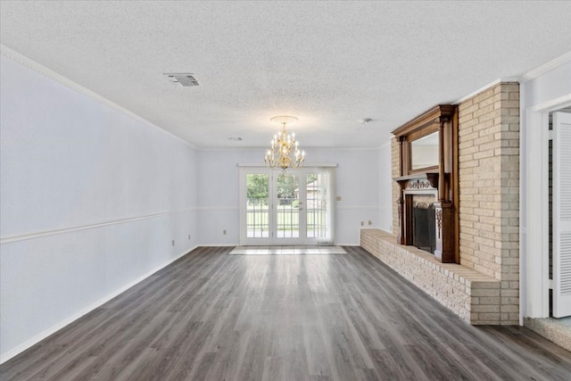 unfurnished living room featuring a textured ceiling, crown molding, a notable chandelier, a fireplace, and dark hardwood / wood-style floors