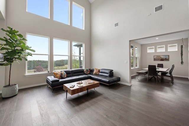 living room with a wealth of natural light, a towering ceiling, and dark wood-type flooring