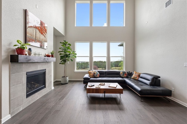 living room featuring dark wood-type flooring, a high ceiling, and a tiled fireplace