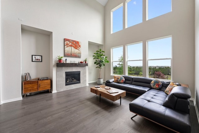 living room featuring dark hardwood / wood-style flooring, a towering ceiling, and a tile fireplace