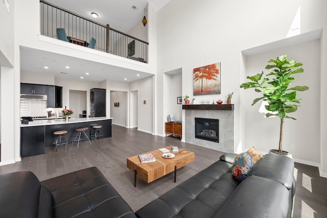 living room with a high ceiling, dark hardwood / wood-style flooring, and a tiled fireplace