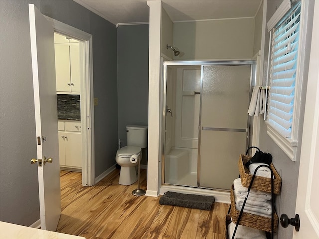 bathroom featuring tasteful backsplash, an enclosed shower, wood-type flooring, toilet, and ornamental molding