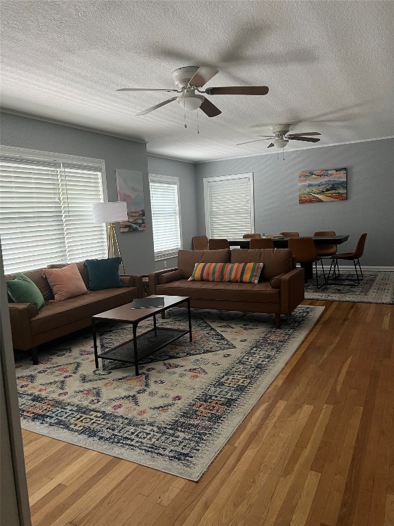 living room featuring ceiling fan, a textured ceiling, and wood-type flooring