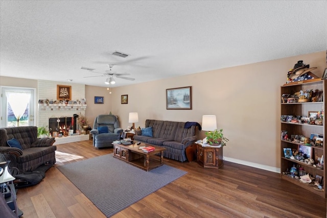 living room with hardwood / wood-style flooring, a brick fireplace, ceiling fan, and a textured ceiling