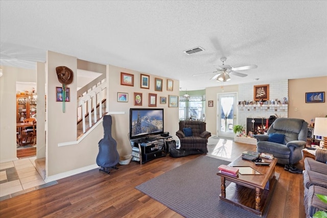 living room with ceiling fan, tile flooring, a textured ceiling, and a brick fireplace