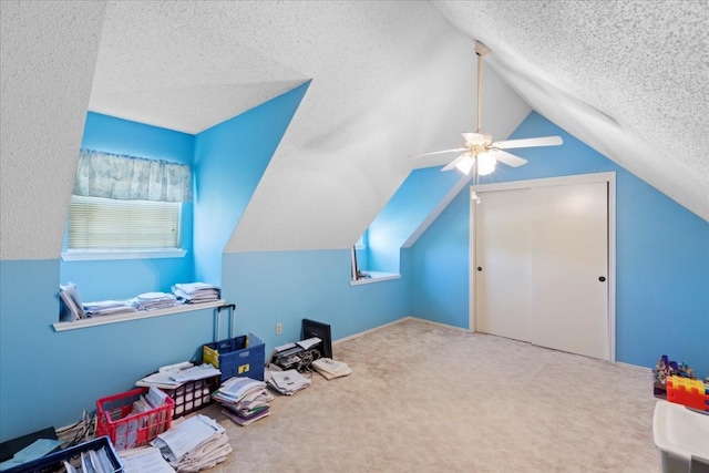 recreation room with vaulted ceiling, carpet, ceiling fan, and a textured ceiling