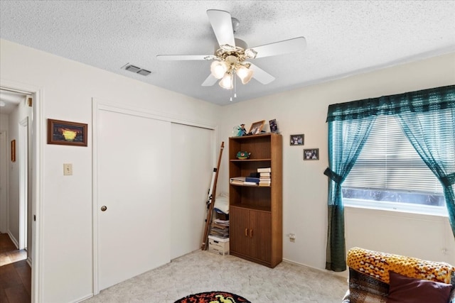 carpeted bedroom with ceiling fan, a closet, and a textured ceiling