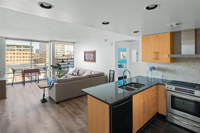 kitchen featuring kitchen peninsula, stainless steel range with gas stovetop, dishwasher, wall chimney range hood, and sink