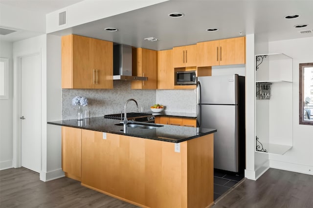 kitchen featuring kitchen peninsula, stainless steel appliances, dark hardwood / wood-style floors, dark stone countertops, and wall chimney range hood