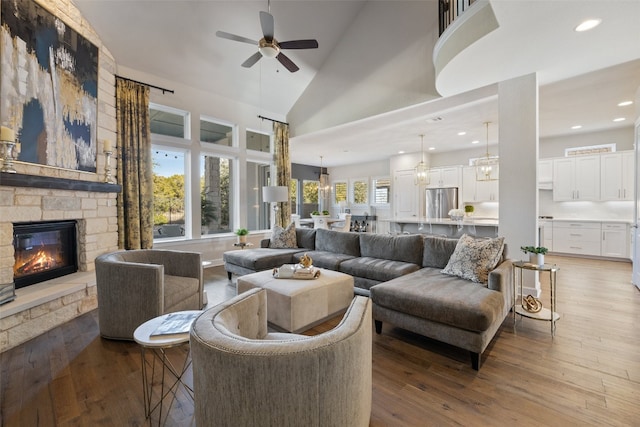 living room featuring a fireplace, ceiling fan, wood-type flooring, and high vaulted ceiling