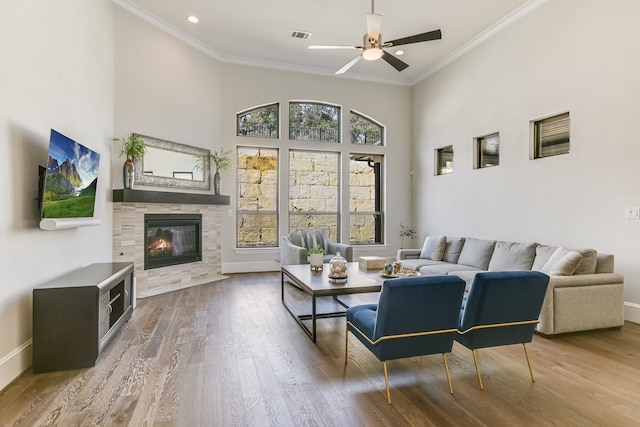 living room featuring wood-type flooring, a fireplace, ornamental molding, and ceiling fan