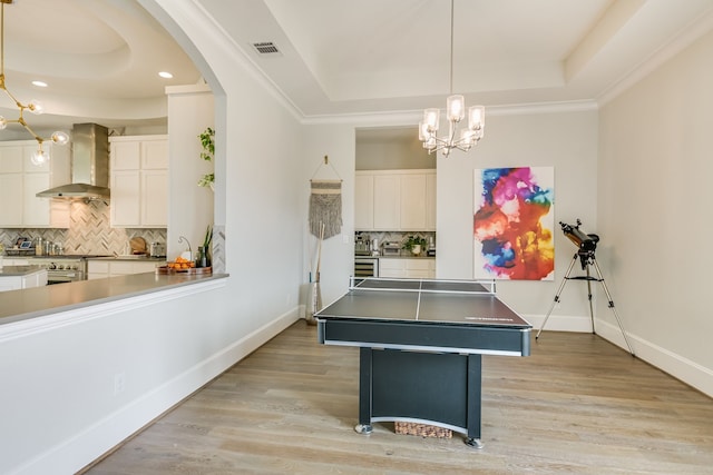 game room featuring a raised ceiling, an inviting chandelier, light wood-type flooring, and crown molding