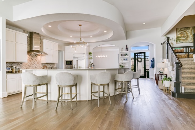 kitchen featuring white cabinets, wall chimney range hood, a tray ceiling, and pendant lighting