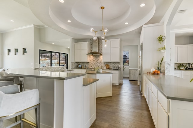 kitchen with a raised ceiling, hanging light fixtures, wall chimney exhaust hood, a spacious island, and white cabinetry