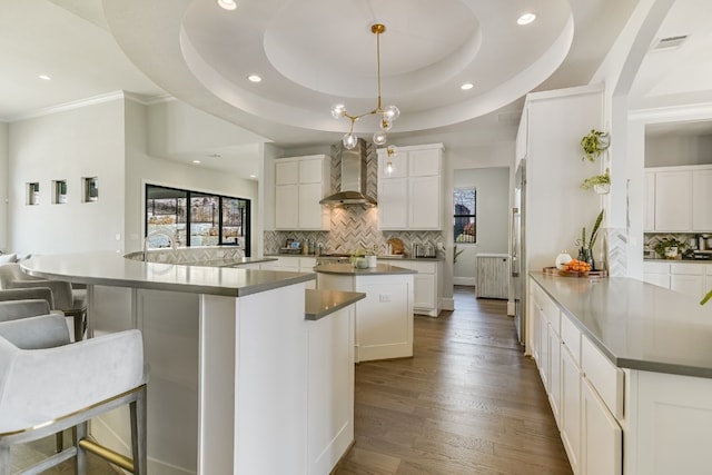 kitchen with a spacious island, a breakfast bar, decorative light fixtures, wall chimney range hood, and white cabinetry