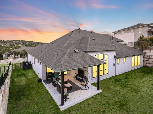 back house at dusk featuring a patio, an outdoor living space, and a lawn