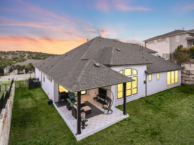 back of house at dusk with a patio, a fenced backyard, a shingled roof, outdoor lounge area, and a yard