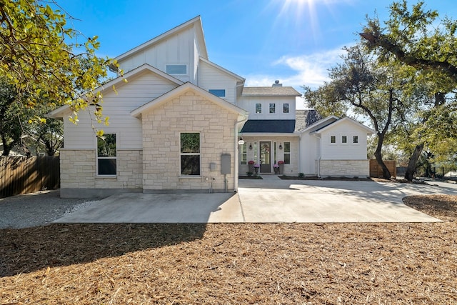 view of front of property featuring stone siding, fence, board and batten siding, and a patio