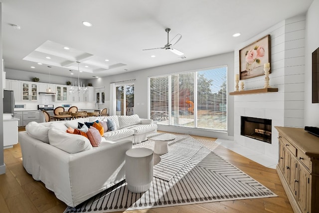 living room with a tiled fireplace, ceiling fan, light hardwood / wood-style floors, and coffered ceiling