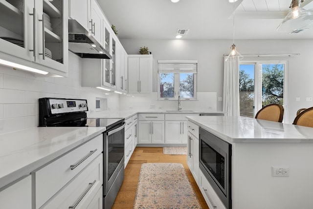 kitchen featuring under cabinet range hood, white cabinets, appliances with stainless steel finishes, a kitchen bar, and glass insert cabinets