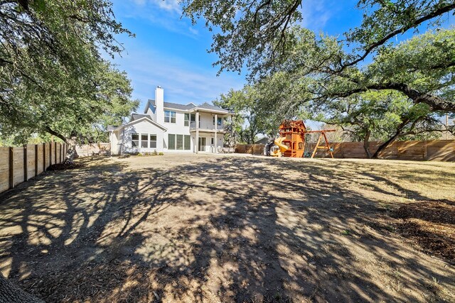 back of property with a chimney, a playground, and a fenced backyard