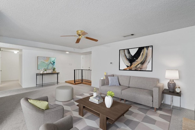 living room featuring visible vents, a ceiling fan, carpet flooring, and a textured ceiling