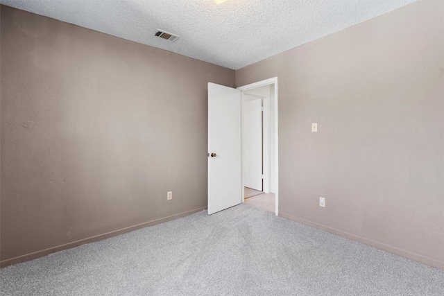 spare room with a textured ceiling, carpet, visible vents, and baseboards