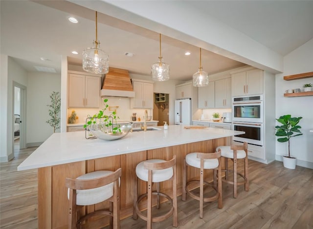 kitchen featuring white appliances, premium range hood, decorative light fixtures, and a large island