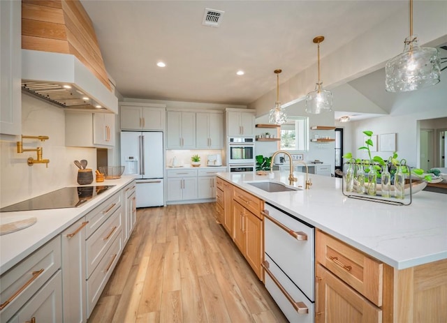 kitchen with sink, white fridge with ice dispenser, white cabinetry, black electric stovetop, and a spacious island