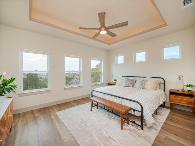 bedroom featuring light wood-type flooring, a raised ceiling, and ceiling fan