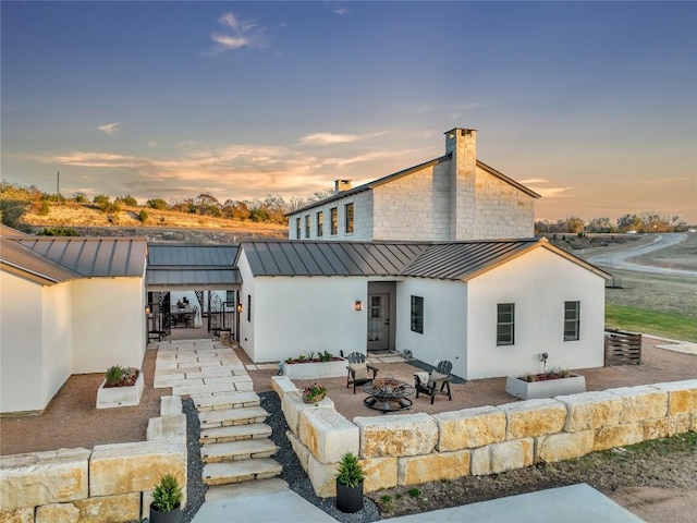 view of front of property with a standing seam roof, a patio, a fire pit, metal roof, and a chimney