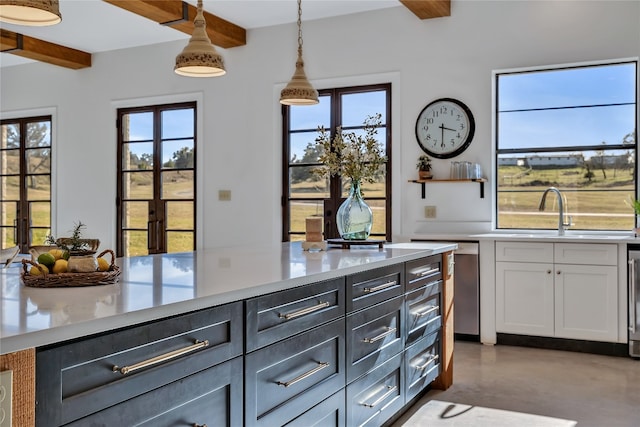 kitchen featuring a healthy amount of sunlight, hanging light fixtures, concrete floors, beam ceiling, and sink