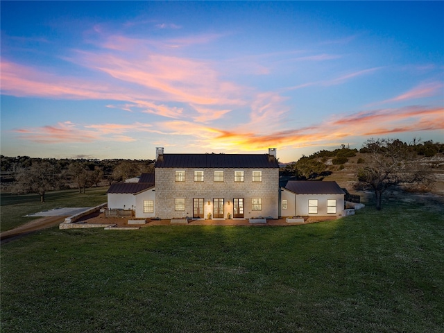 back house at dusk featuring a lawn