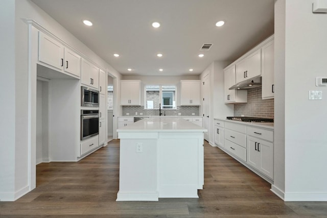 kitchen featuring white cabinetry, backsplash, stainless steel appliances, a kitchen island, and dark wood-type flooring