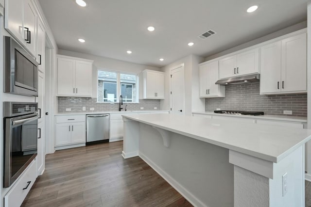 kitchen featuring appliances with stainless steel finishes, backsplash, dark hardwood / wood-style flooring, and white cabinetry