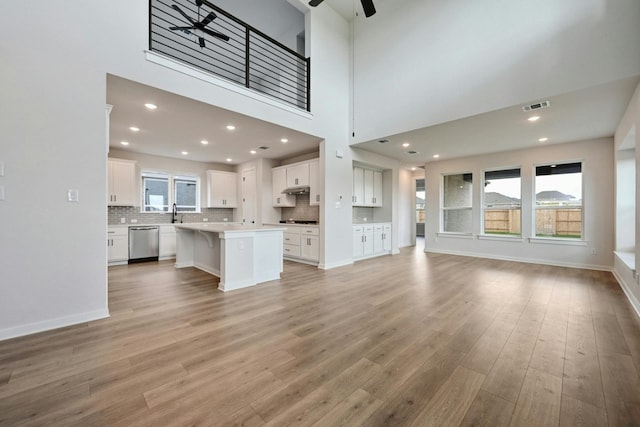 unfurnished living room with ceiling fan, a towering ceiling, and light wood-type flooring