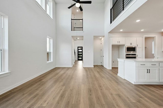 unfurnished living room featuring a towering ceiling, light hardwood / wood-style flooring, and ceiling fan