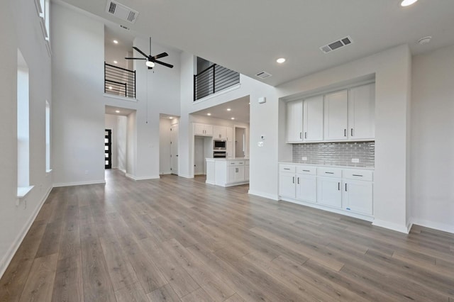 unfurnished living room featuring light wood-type flooring, a high ceiling, and ceiling fan