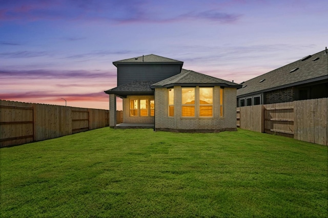 back house at dusk featuring a lawn