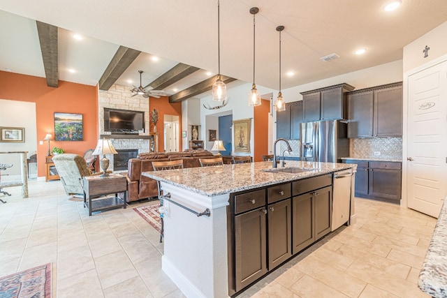 kitchen featuring appliances with stainless steel finishes, beamed ceiling, ceiling fan, a fireplace, and dark brown cabinets