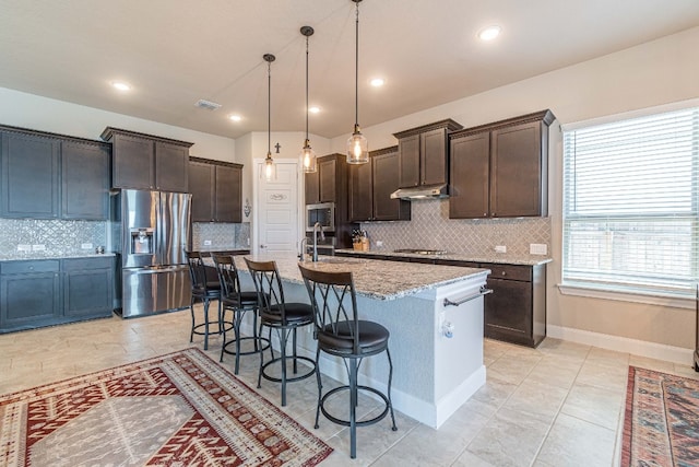 kitchen featuring decorative light fixtures, backsplash, stainless steel appliances, and light stone countertops