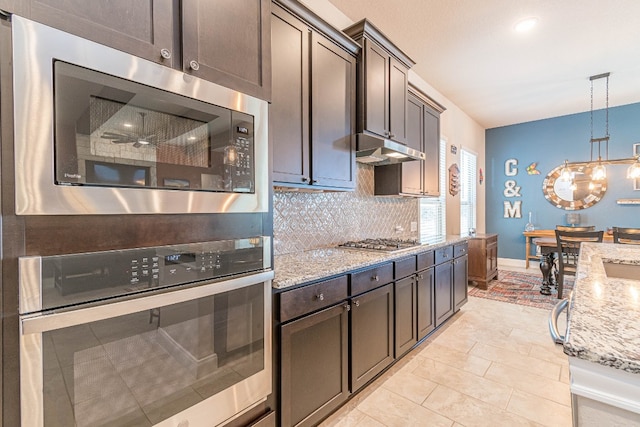 kitchen featuring dark brown cabinetry, pendant lighting, stainless steel appliances, light stone countertops, and backsplash