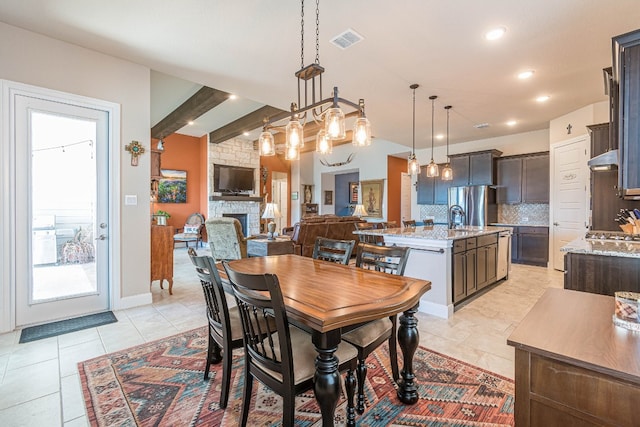 dining room featuring sink, light tile floors, a chandelier, beamed ceiling, and a stone fireplace