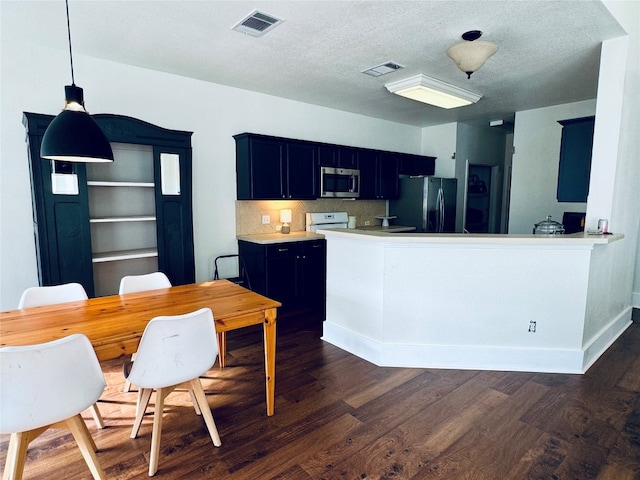 kitchen featuring dark wood-type flooring, stainless steel appliances, kitchen peninsula, pendant lighting, and a textured ceiling