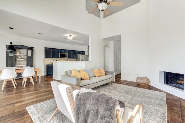 living room featuring a high ceiling, ceiling fan, and dark wood-type flooring