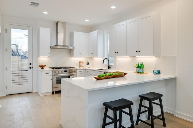 kitchen featuring wall chimney range hood, white cabinets, stainless steel range, and sink