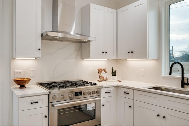 kitchen with stainless steel stove, sink, wall chimney exhaust hood, and white cabinetry