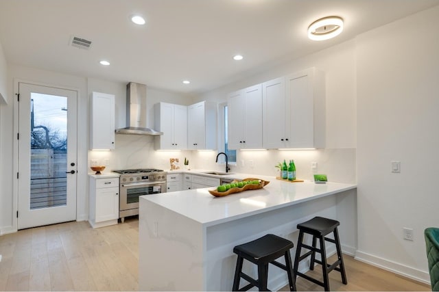 kitchen featuring wall chimney exhaust hood, a kitchen bar, white cabinets, and light wood-type flooring